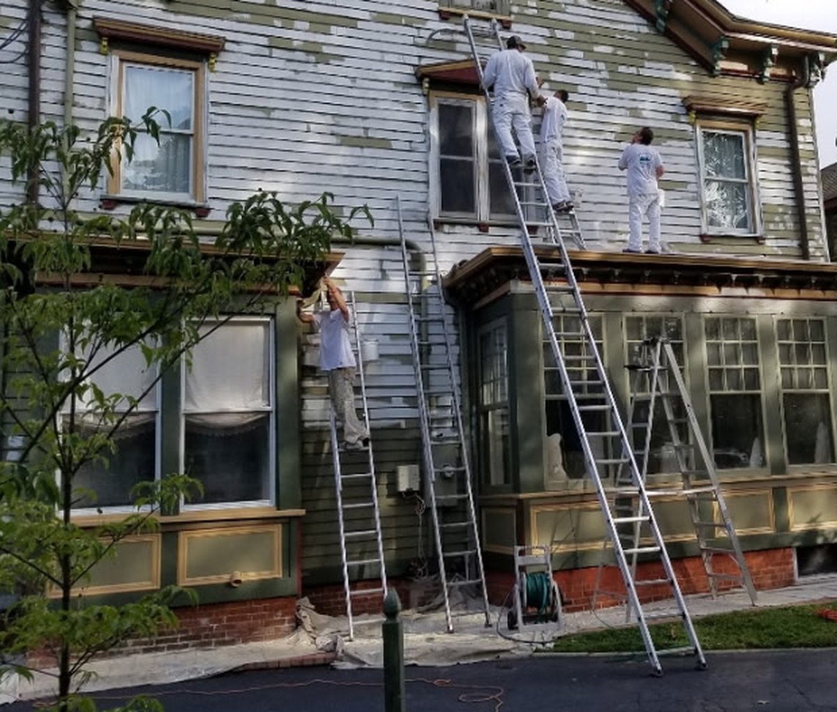 Victorian house mid-project with the crew on ladders and the siding stripped back